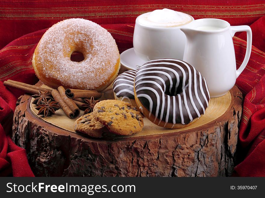 Donut with chocolate and sugar on wooden stump with cinnamon and background with red cloth. Donut with chocolate and sugar on wooden stump with cinnamon and background with red cloth