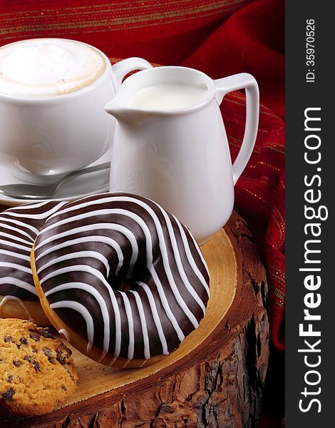 Cappuccino with milk and chocolate donut on wooden stump and background with red cloth. Cappuccino with milk and chocolate donut on wooden stump and background with red cloth