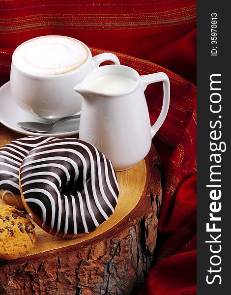 Cappuccino with milk and chocolate donut on wooden stump and background with red cloth. Cappuccino with milk and chocolate donut on wooden stump and background with red cloth