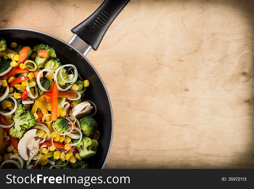 Frying vegetables in pan close-up on light wooden background. Space for text. Frying vegetables in pan close-up on light wooden background. Space for text