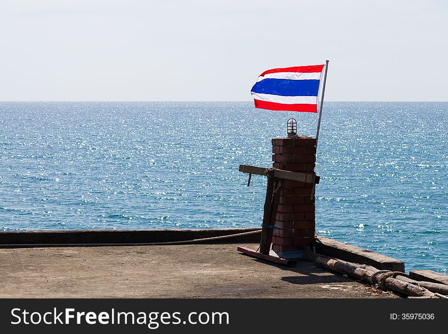Flag of Thailand on small pole in front of sea.