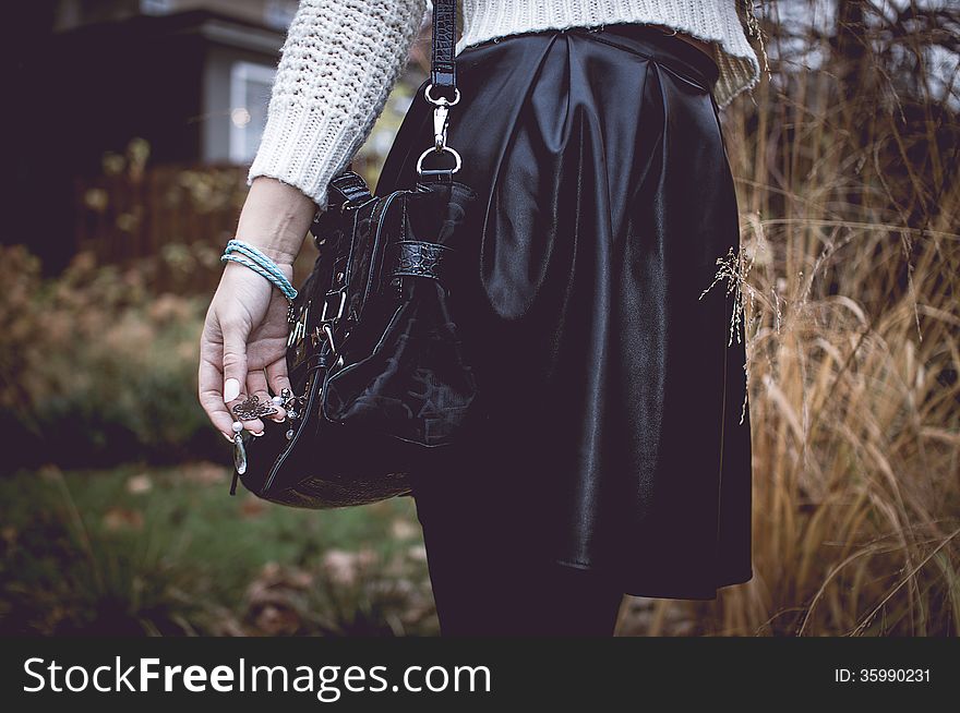 Young woman with silver jewelary on hand in white sweater with black bag in black skirt. Young woman with silver jewelary on hand in white sweater with black bag in black skirt