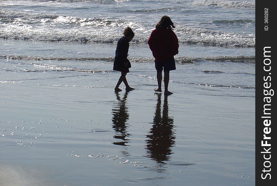 Two young girls cautiously toe the water at the seaside. Two young girls cautiously toe the water at the seaside.