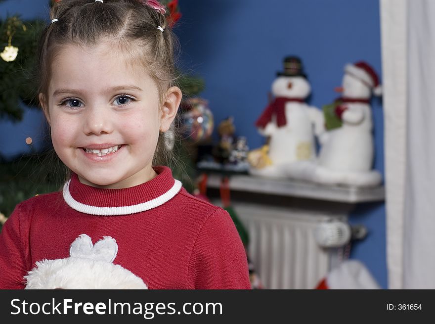 Little girl stands in front of a Christmas tree holding a teddy bear-Christmas snowmen are in the background. Little girl stands in front of a Christmas tree holding a teddy bear-Christmas snowmen are in the background