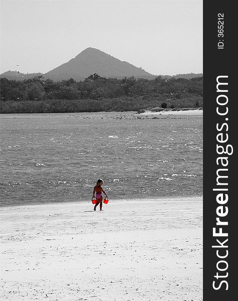 A little girl strolls along the beach with her red buckets