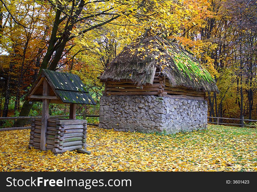 A wooden rural cottage with a thatch roof on which grows green moss in the forest Alongside wooden well