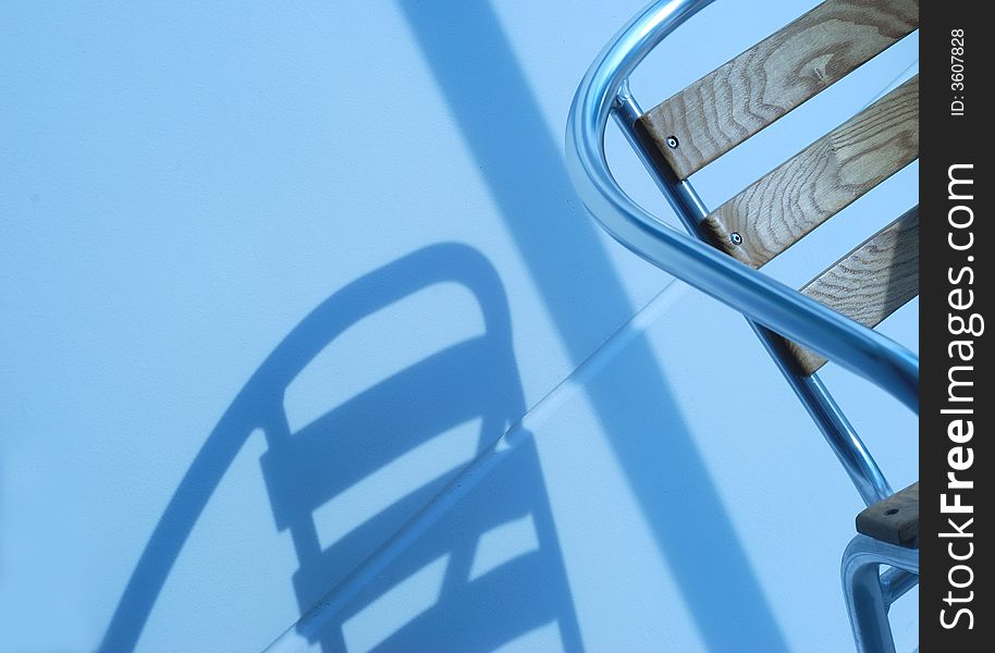 A chair and it's blue shadow on a white wall and concrete floor. A chair and it's blue shadow on a white wall and concrete floor