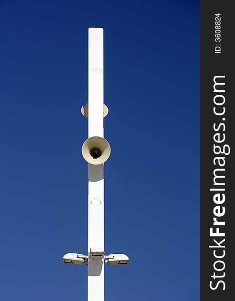 A modern loudspeaker and light pole against the dark blue sky