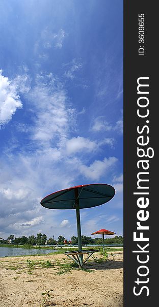 Vertical panorama of the river beach with red parasols in a country. Vertical panorama of the river beach with red parasols in a country