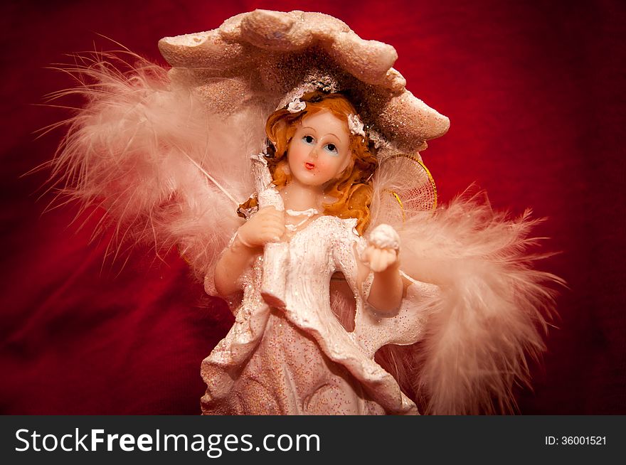 Portrait of a handmade angel figurine on a stylish red background.