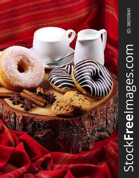 Donut with chocolate and sugar on wooden stump with cinnamon and background with red cloth. Donut with chocolate and sugar on wooden stump with cinnamon and background with red cloth