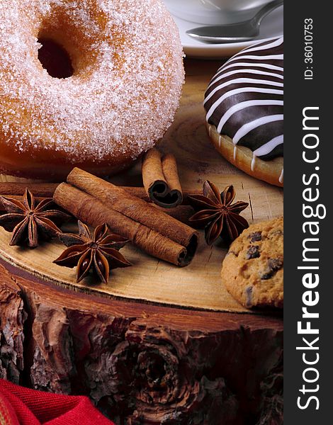 Block of wood with a chocolate donut and donut with sugar in the foreground cinnamon and star anise. Block of wood with a chocolate donut and donut with sugar in the foreground cinnamon and star anise