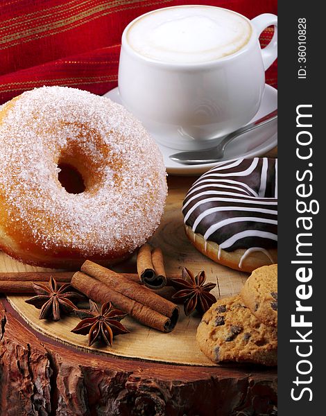 Donut with chocolate and sugar on wooden stump with cinnamon and background with red cloth. Donut with chocolate and sugar on wooden stump with cinnamon and background with red cloth