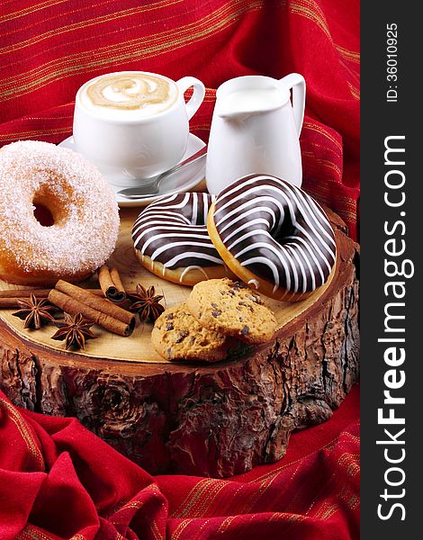 Donut with chocolate and sugar on wooden stump with cinnamon and background with red cloth. Donut with chocolate and sugar on wooden stump with cinnamon and background with red cloth