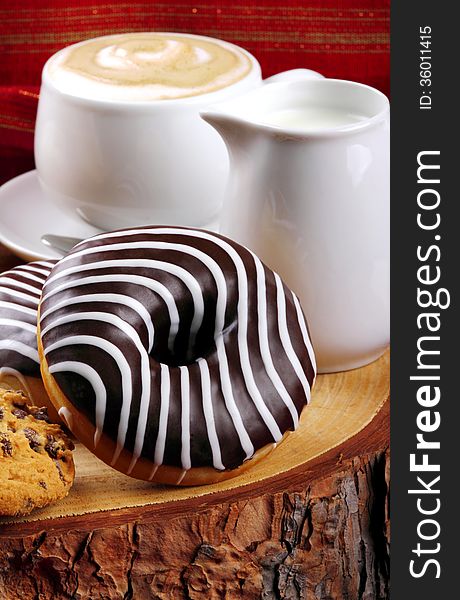 Cappuccino with milk and chocolate donut on wooden stump and background with red cloth. Cappuccino with milk and chocolate donut on wooden stump and background with red cloth