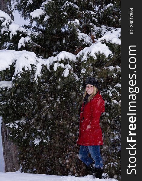 Blonde female wearing a red coat and black hat in front of trees covered in snow. Blonde female wearing a red coat and black hat in front of trees covered in snow.