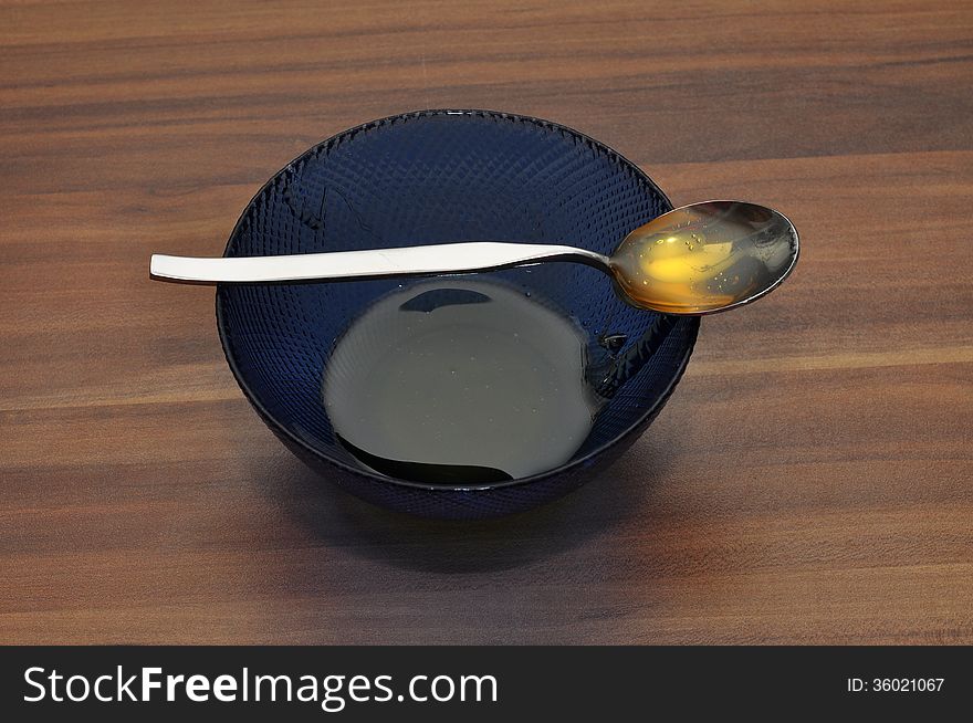 A small cup of honey with a spoon also filled with honey on a wooden table. A small cup of honey with a spoon also filled with honey on a wooden table.