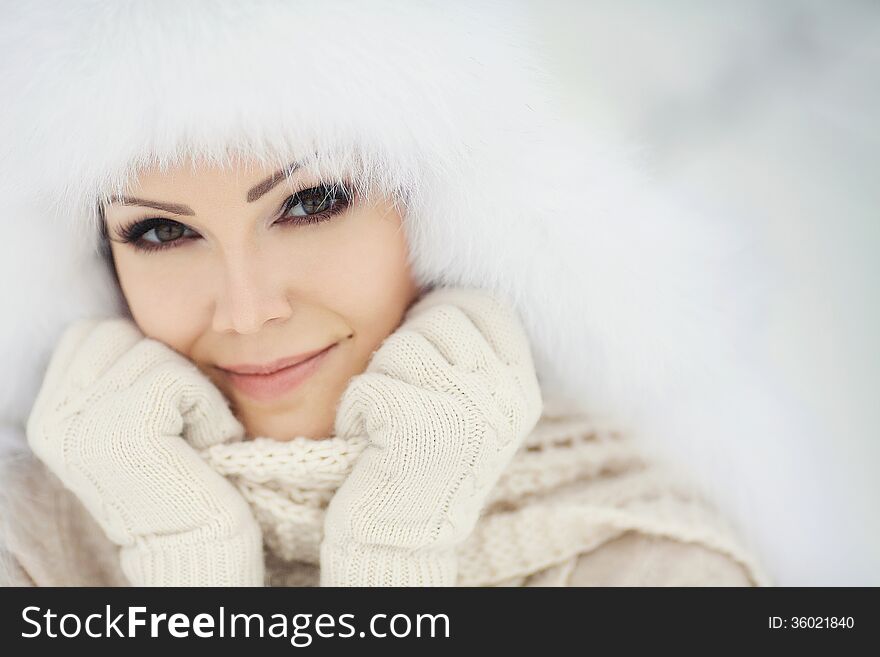 Winter portrait of beautiful smiling woman with snowflakes in white furs