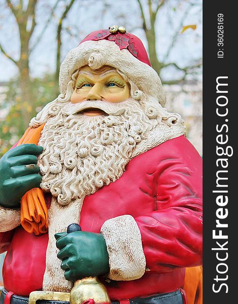 Statue of santa claus dressed in red with beard and hat with trees and sky behind