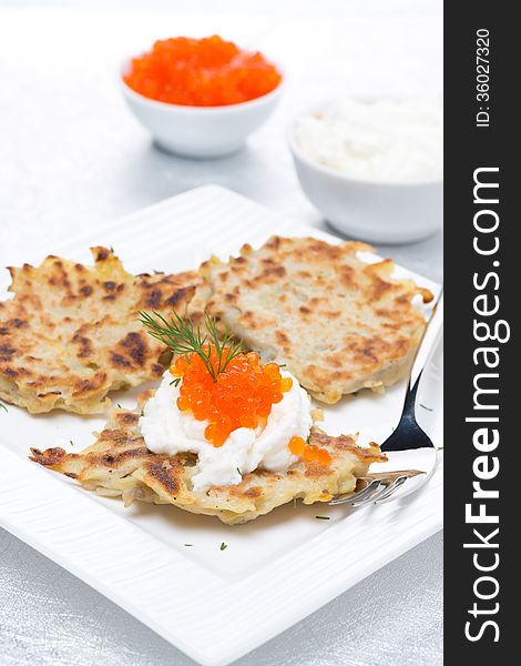 Potato pancakes with red caviar and sour cream, vertical, close-up
