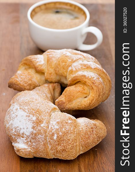 Two fresh croissants and coffee on a wooden background, close-up