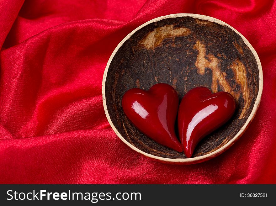Two hearts in a bowl of coconut on red satin background, close-up