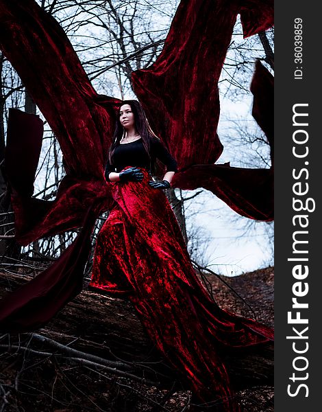 Mysterious Woman Or Witch In Long Red Dress Standing In Dark Forest With Flying Fabric