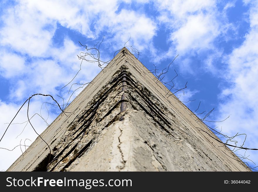 Fragment of old obsolete reinforced concrete structures with rusty iron rods outside. The pyramid of concrete looks at the blue sky.