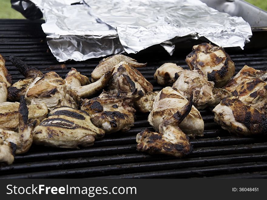 Chicken on an outdoor grill with a silver foil covered pan in the background. Chicken on an outdoor grill with a silver foil covered pan in the background