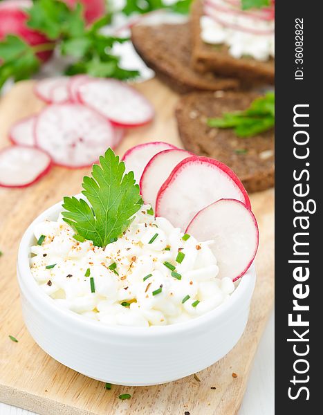 Soft cottage cheese with radish and chives in a bowl on wooden board