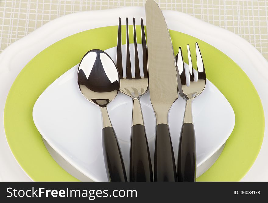 Elegant Table Setting with Spoon, Fork, Table Knife and Dessert Fork on White and Green Plates closeup