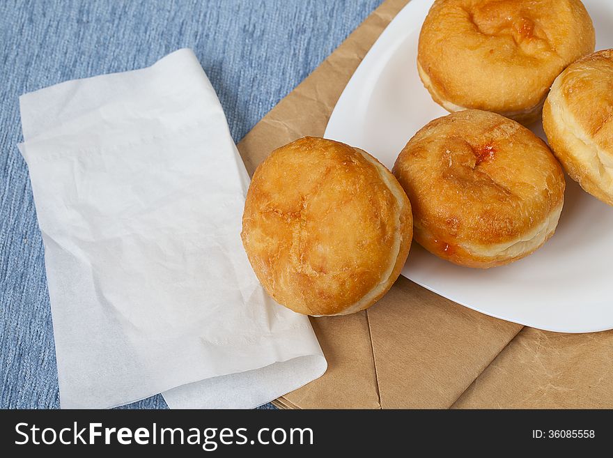 Jelly filled Bismark doughnuts on white plate over craft packet with napkin. Jelly filled Bismark doughnuts on white plate over craft packet with napkin