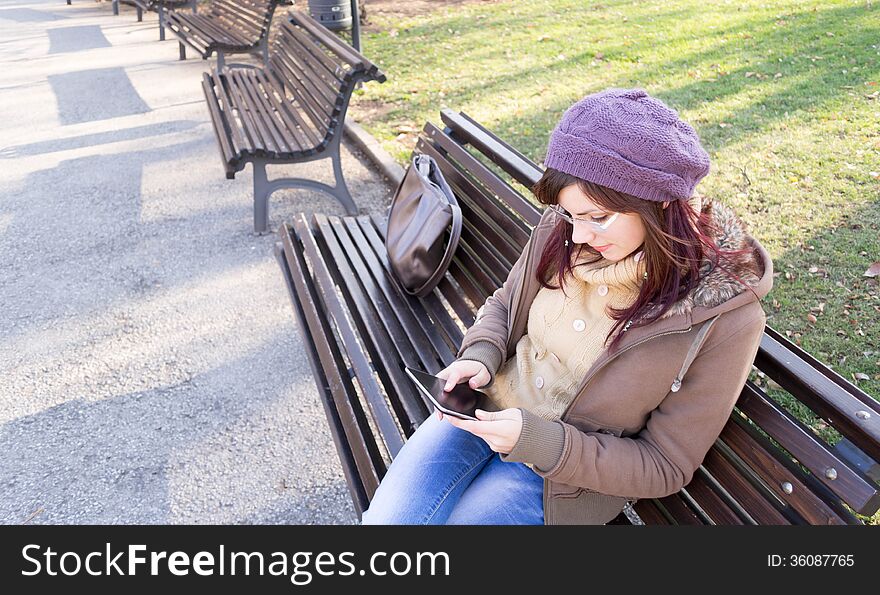 Young girl sitting on a bench and using her digital tablet outdoor in a park. Young girl sitting on a bench and using her digital tablet outdoor in a park.