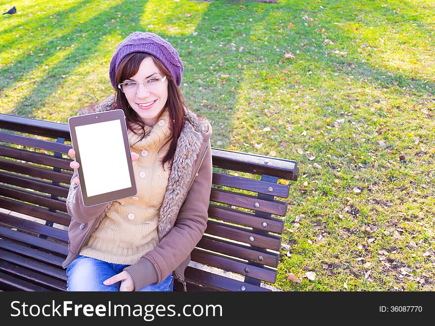 Young girl sitting on a bench and showing digital tablet outdoor in a park. Young girl sitting on a bench and showing digital tablet outdoor in a park.