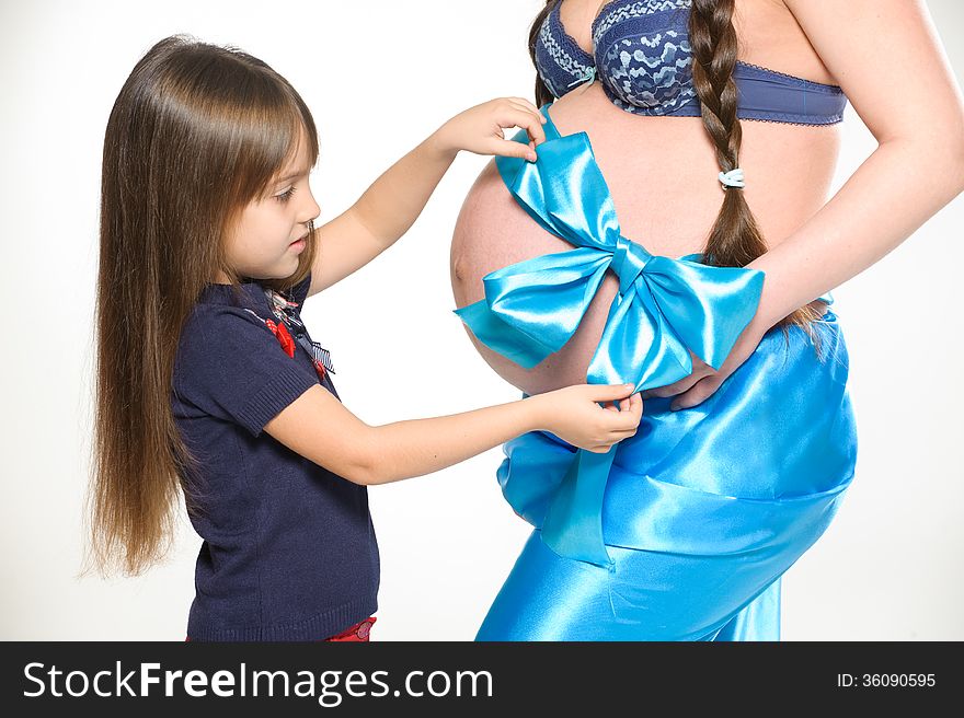 Girl ties a bow on a belly of a pregnant woman. Girl ties a bow on a belly of a pregnant woman