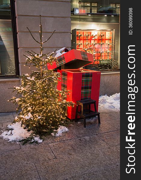 Small christmas tree snow covered in a small square of Zurich with a gift box behind