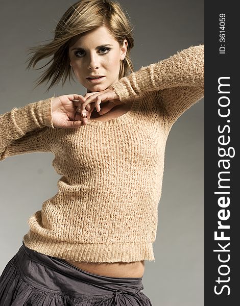 Beautiful blonde model wearing light sweater and grey skirt posing on grey background