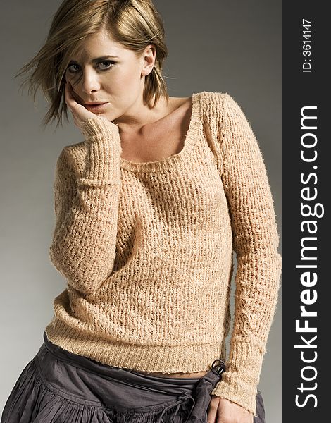 Beautiful blonde model wearing light sweater and grey skirt posing on grey background