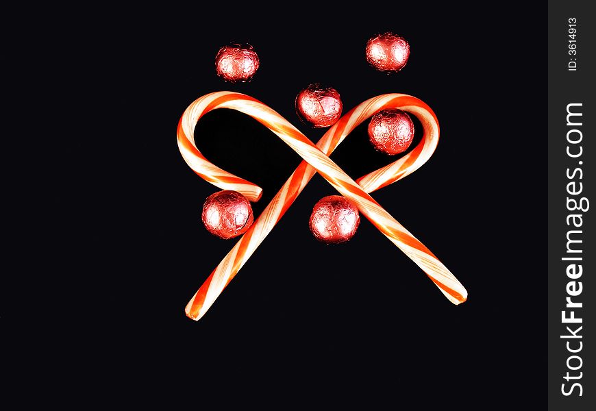 Candy canes and foil covered chocolates against a black background. Candy canes and foil covered chocolates against a black background.