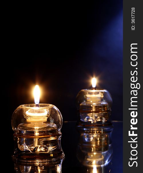 2 burning candles on glass table with dark and blue background