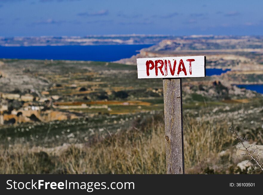 A PRIVAT sign located near a private property in the countryside on the island of Malta. In the blurred background the island of Gozo is visible. A PRIVAT sign located near a private property in the countryside on the island of Malta. In the blurred background the island of Gozo is visible.