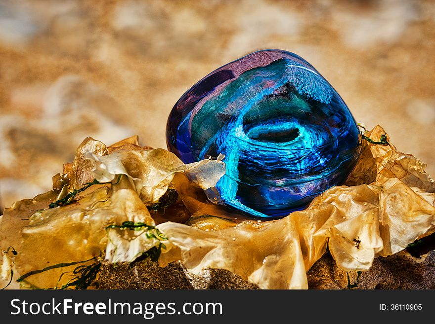 Blue paperweight resting on natural seaweed on sand. Blue paperweight resting on natural seaweed on sand.