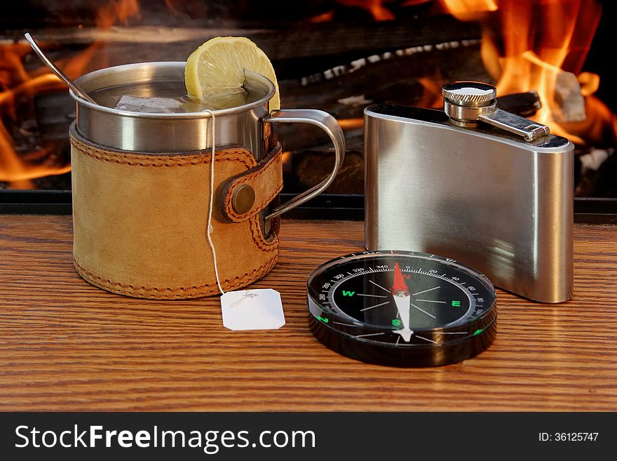Mug of Tea, Hip Flask and a Compass on a Wooden Plank at Campfire. Mug of Tea, Hip Flask and a Compass on a Wooden Plank at Campfire