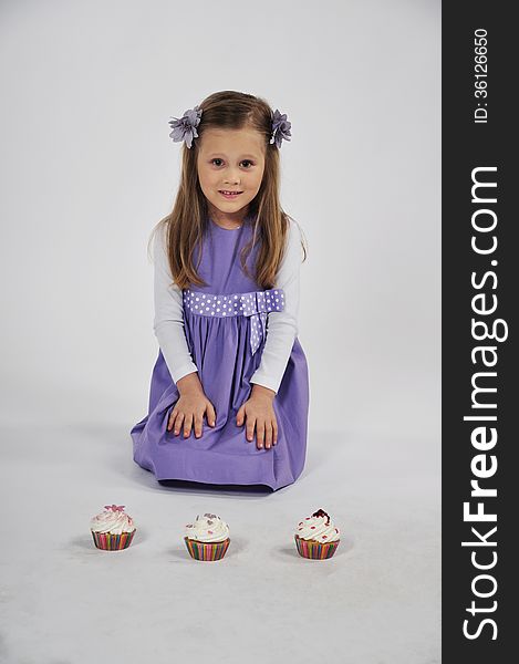A cute little girl is sitting in a studio with three delicious cupcakes in front of her. A cute little girl is sitting in a studio with three delicious cupcakes in front of her.