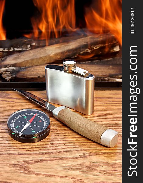 Compass, Hip Flask, and a knife on a Wooden Plank at Campfire. Compass, Hip Flask, and a knife on a Wooden Plank at Campfire