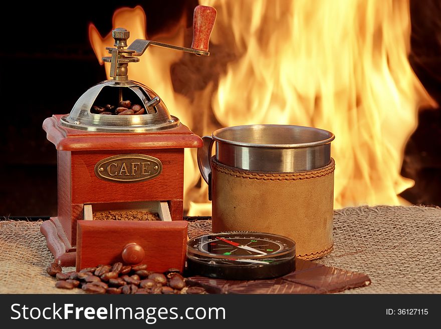 Coffee grinder and mug are near campfire beside them chocolate and compass. Coffee grinder and mug are near campfire beside them chocolate and compass