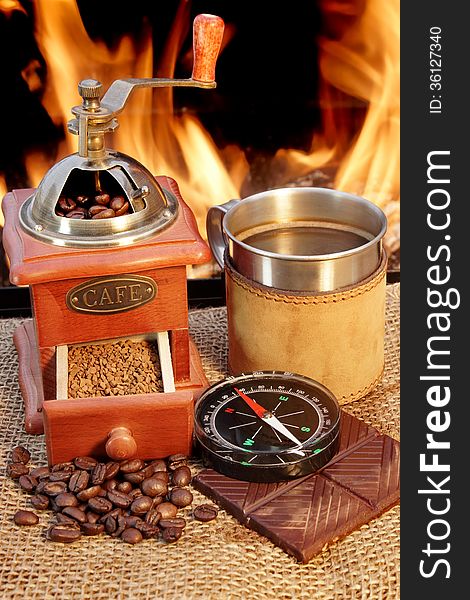 Coffee grinder and mug are near campfire beside them chocolate and compass. Coffee grinder and mug are near campfire beside them chocolate and compass