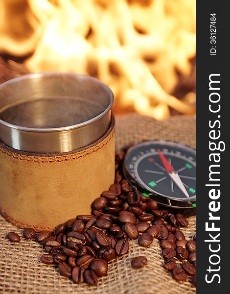 Coffee mug, coffee beans and compass near campfire. Coffee mug, coffee beans and compass near campfire