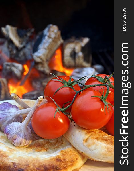 Bread, tomatoes and garlic on the background of hot coals. Bread, tomatoes and garlic on the background of hot coals