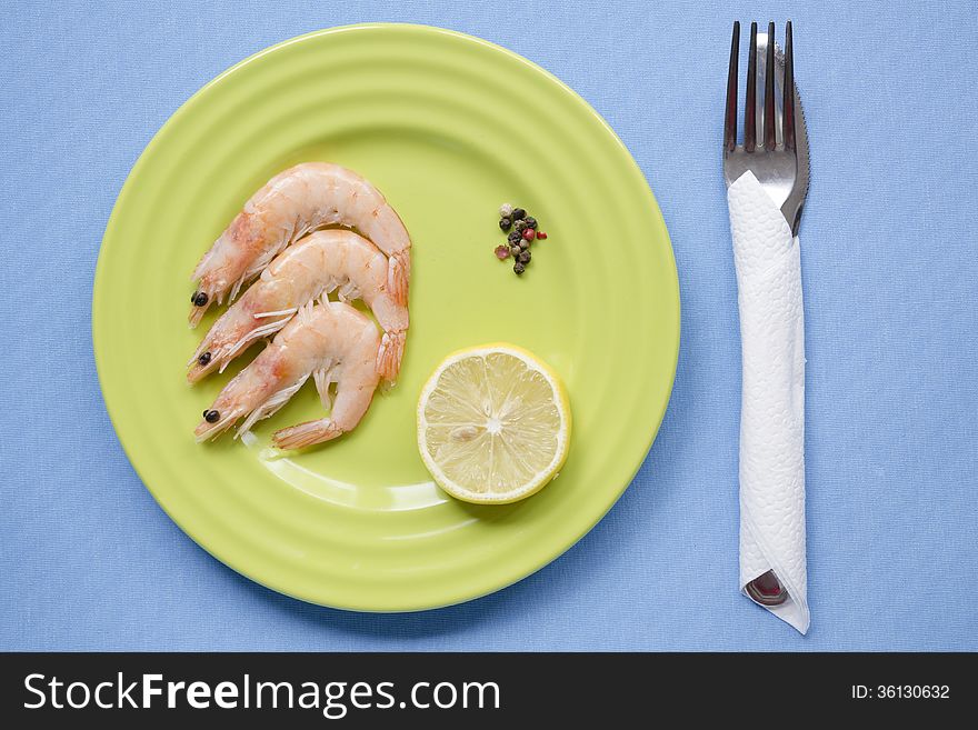Shrimps portion on green plate with lemon slice on blue tablecloth. Shrimps portion on green plate with lemon slice on blue tablecloth